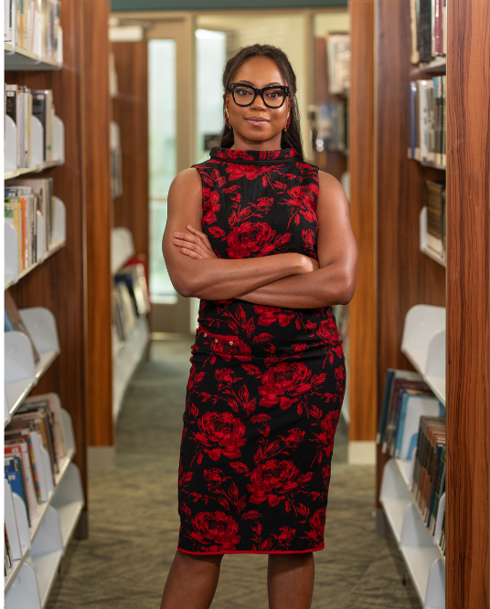 Abbey Fajimolu standing in library with arms crossed